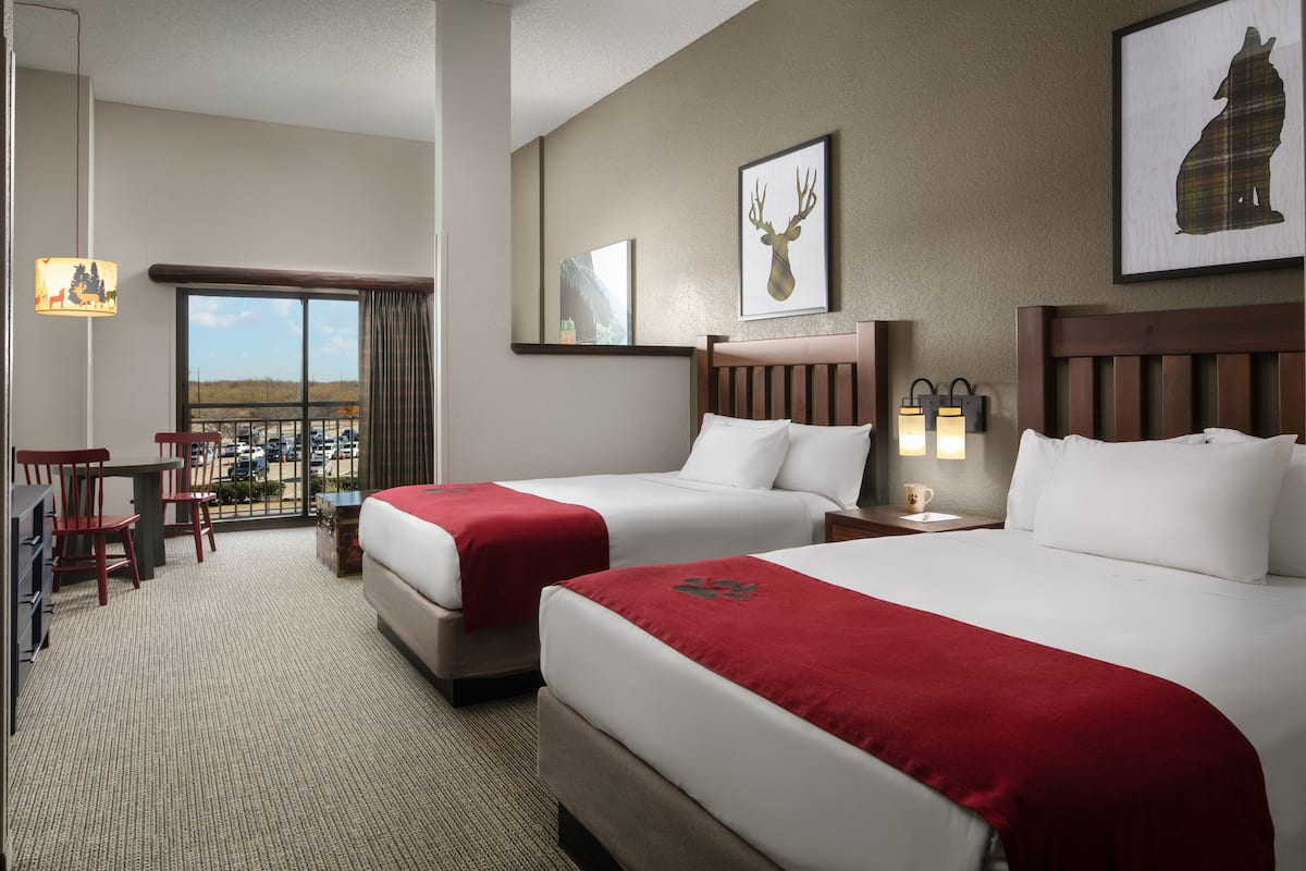 Ein Hotelzimmer mit zwei Betten, einem Schreibtisch, Stühlen und Blick auf die Stadt.