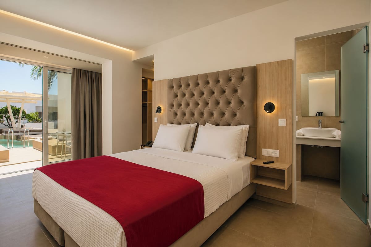 A modern hotel room with a large bed, a built-in vanity, and a sliding glass door to a balcony.