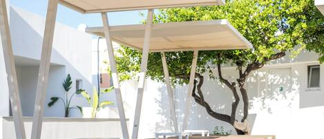 Outdoor seating with white and beige cushions, a pergola, and a tree.