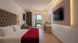 Une chambre d’hôtel moderne, dotée d’un grand lit, d’un bureau, d’une télévision et offrant une vue sur la verdure environnante.