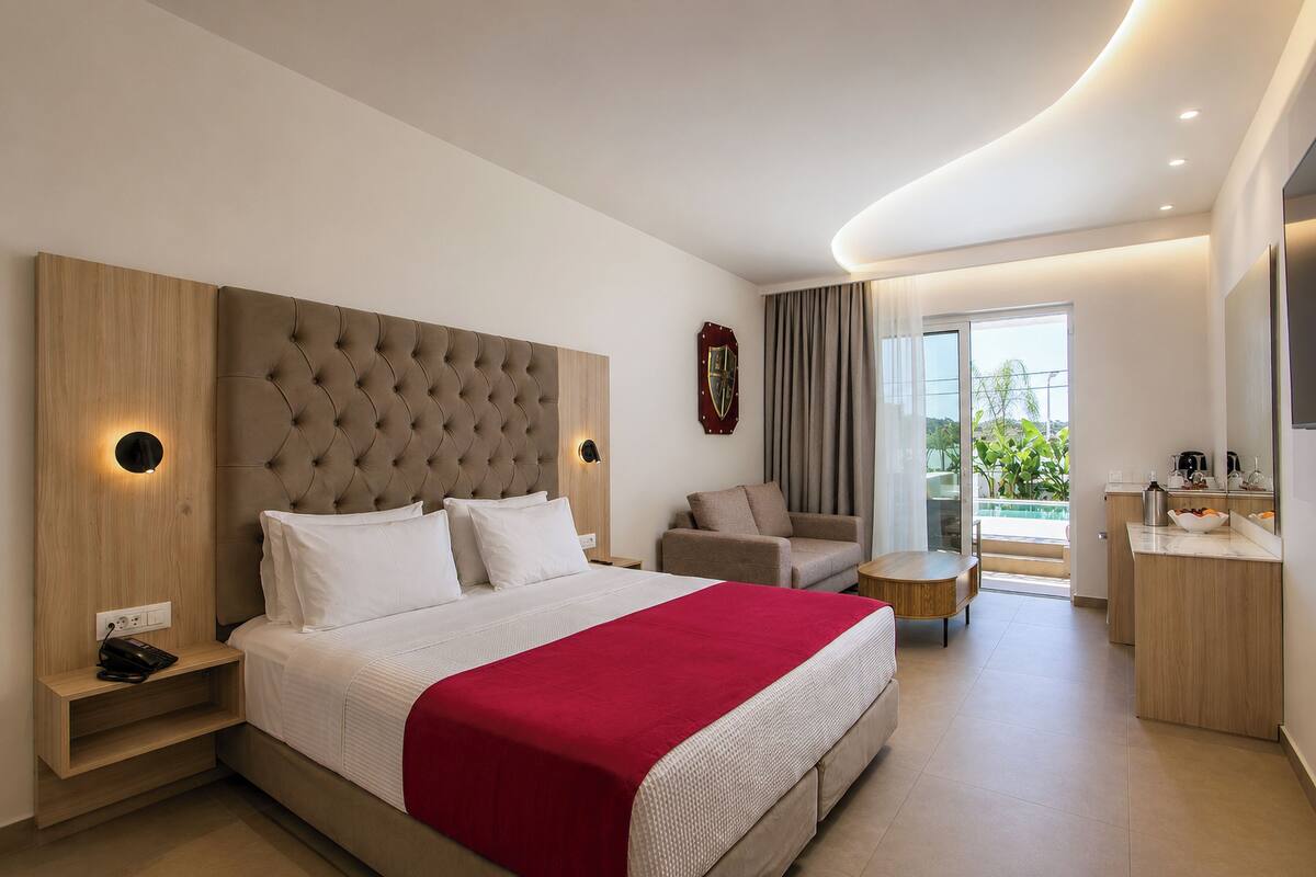 A modern hotel room with a large bed, a seating area, a small table, and a bathroom.