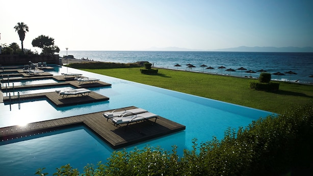 Una piscina con múltiples tumbonas y vista al mar.