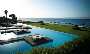 A pool with multiple sun loungers and a view of the sea. - The Ixian Grand & All Suites - Adults Only (Rhodes)