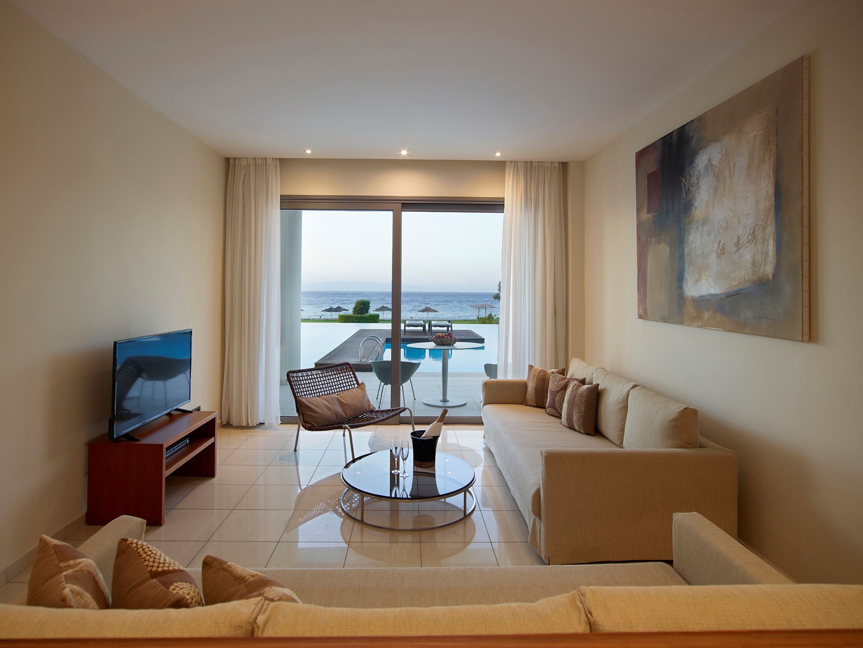 Un salon moderne avec un téléviseur, un canapé, une table basse et une vue sur une piscine et l’océan.