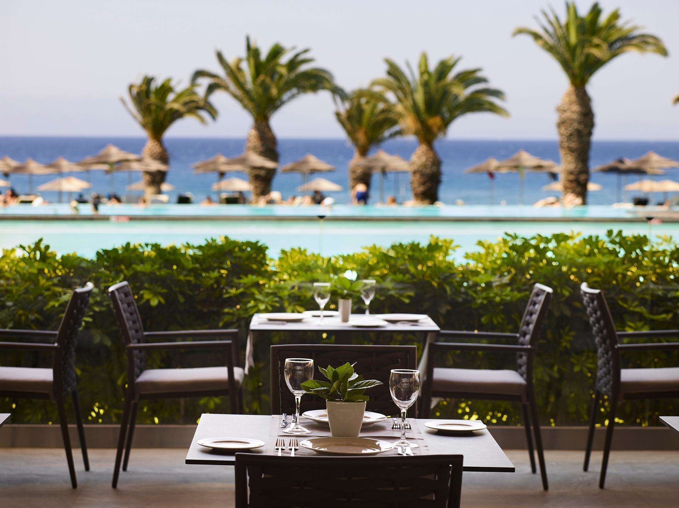 A dining table set for two with a view of a pool and palm trees.