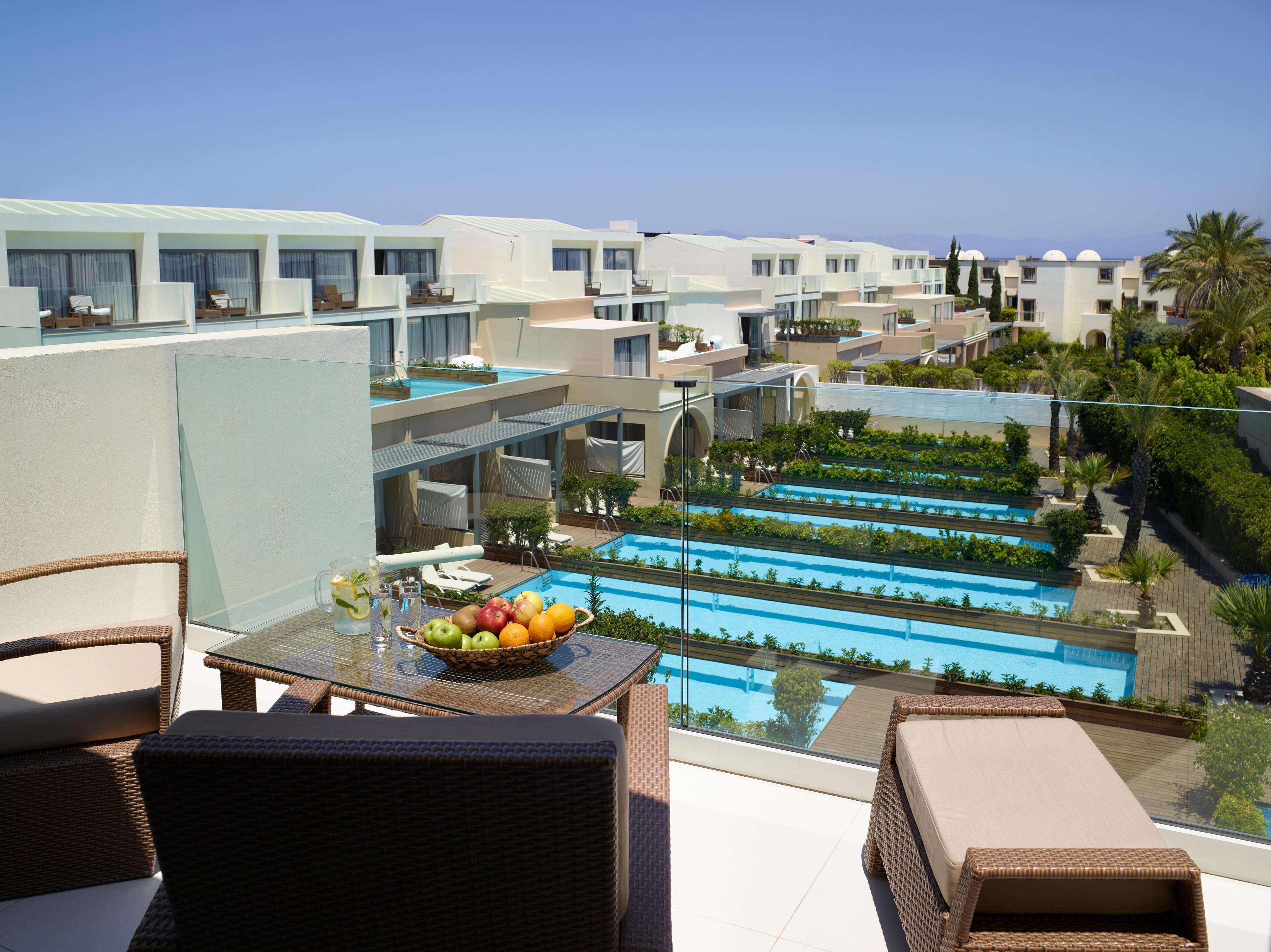 A rooftop pool area with multiple swimming pools, lounge chairs, and a table with a fruit bowl.