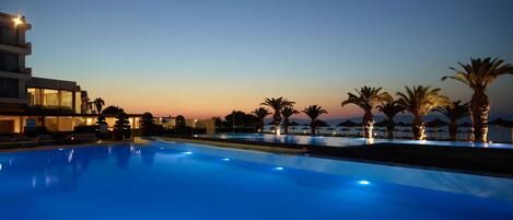 A swimming pool at dusk with a view of a hotel and palm trees.