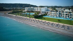 Vista aérea de un hotel costero con playa privada, varias piscinas y un jardín cuidado.
