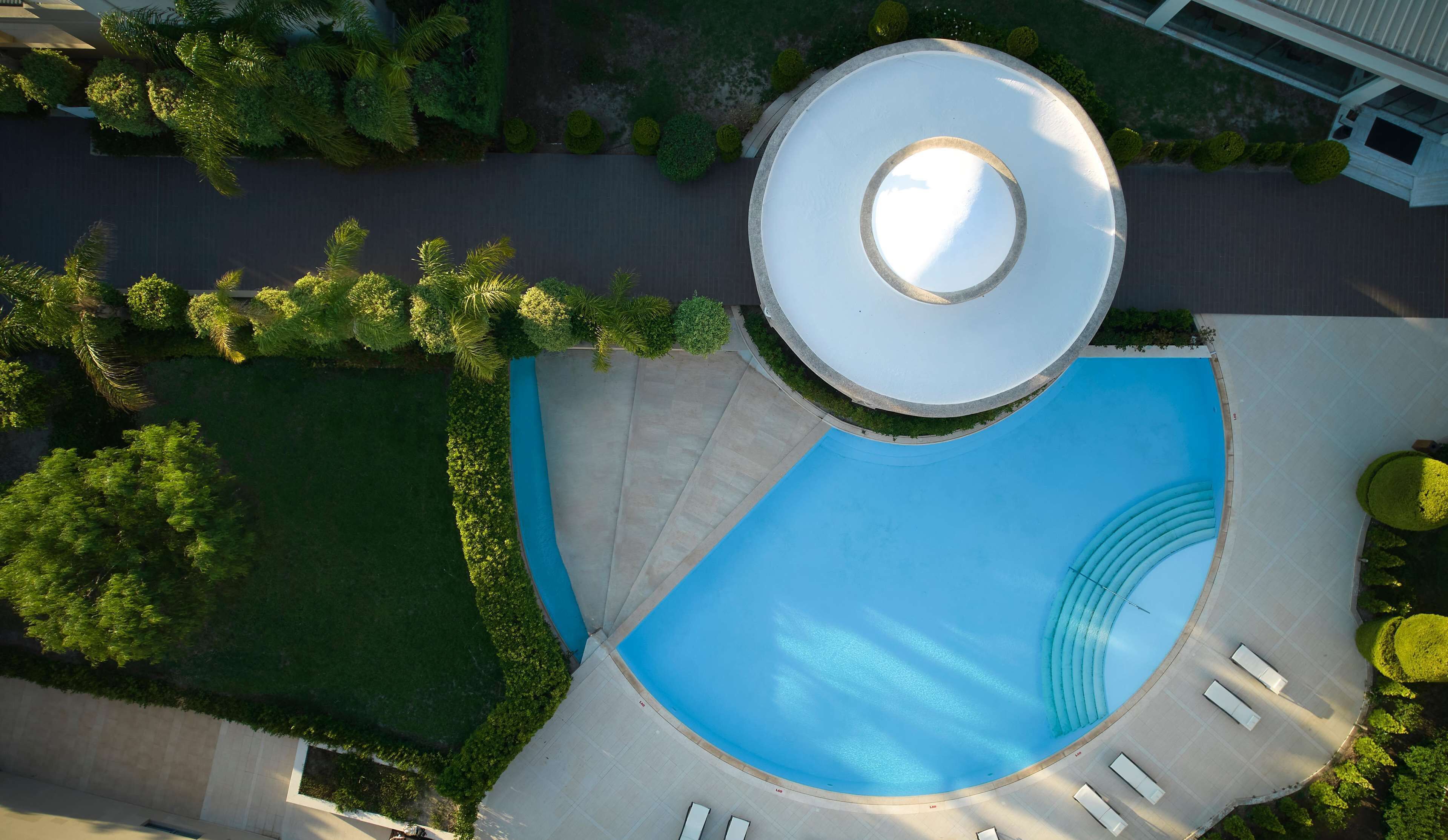 An aerial view of a swimming pool with a circular deck, surrounded by well-manicured lawns and hedges.