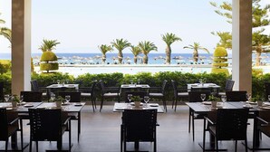 Un área de comedor al aire libre con mesas y sillas, con vista a una piscina y palmeras.