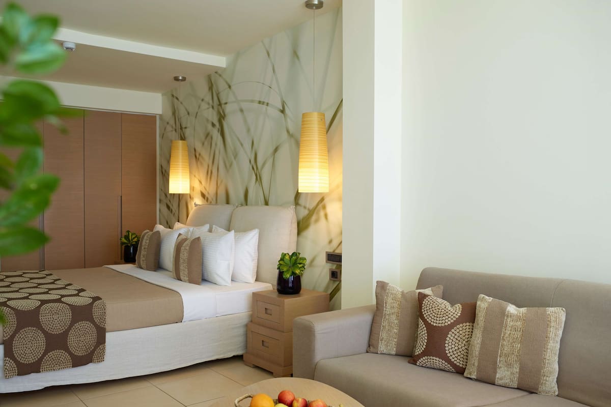 Habitación de hotel con cama, sofá, una mesita con fruta y lámparas de pared.