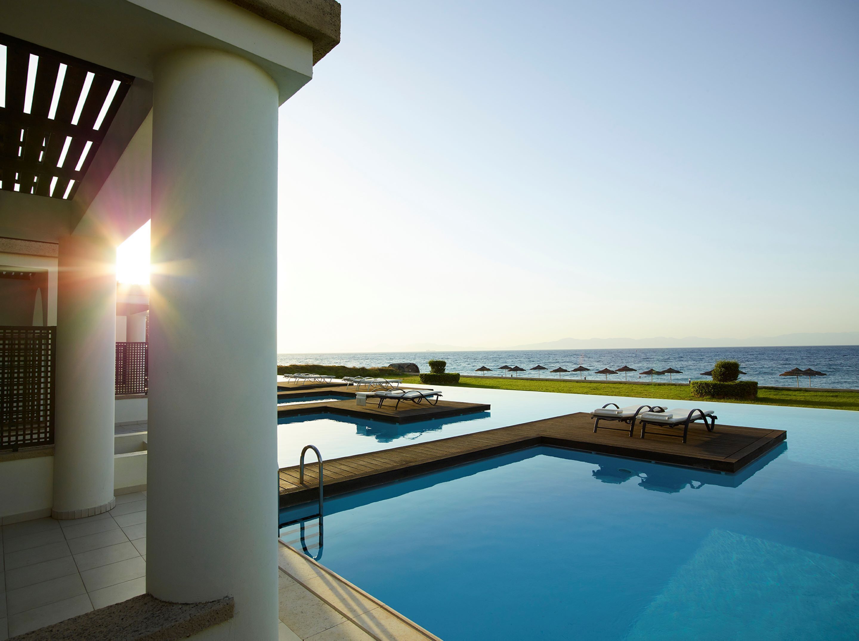A pool area with clear views of the sea, a wooden deck, and lounge chairs.