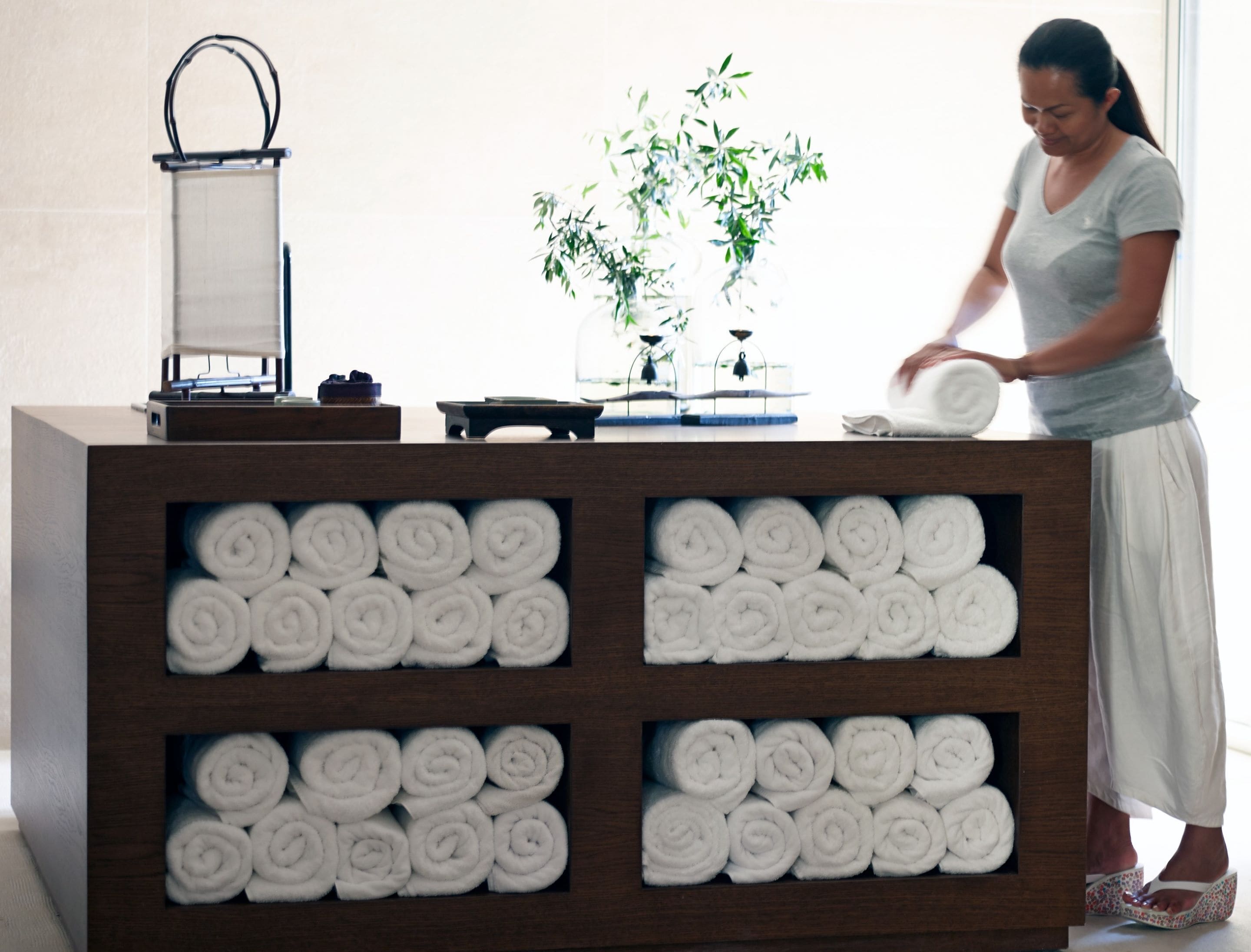 A reception area with a wooden counter displaying rolled towels, a scale, and a small plant.
