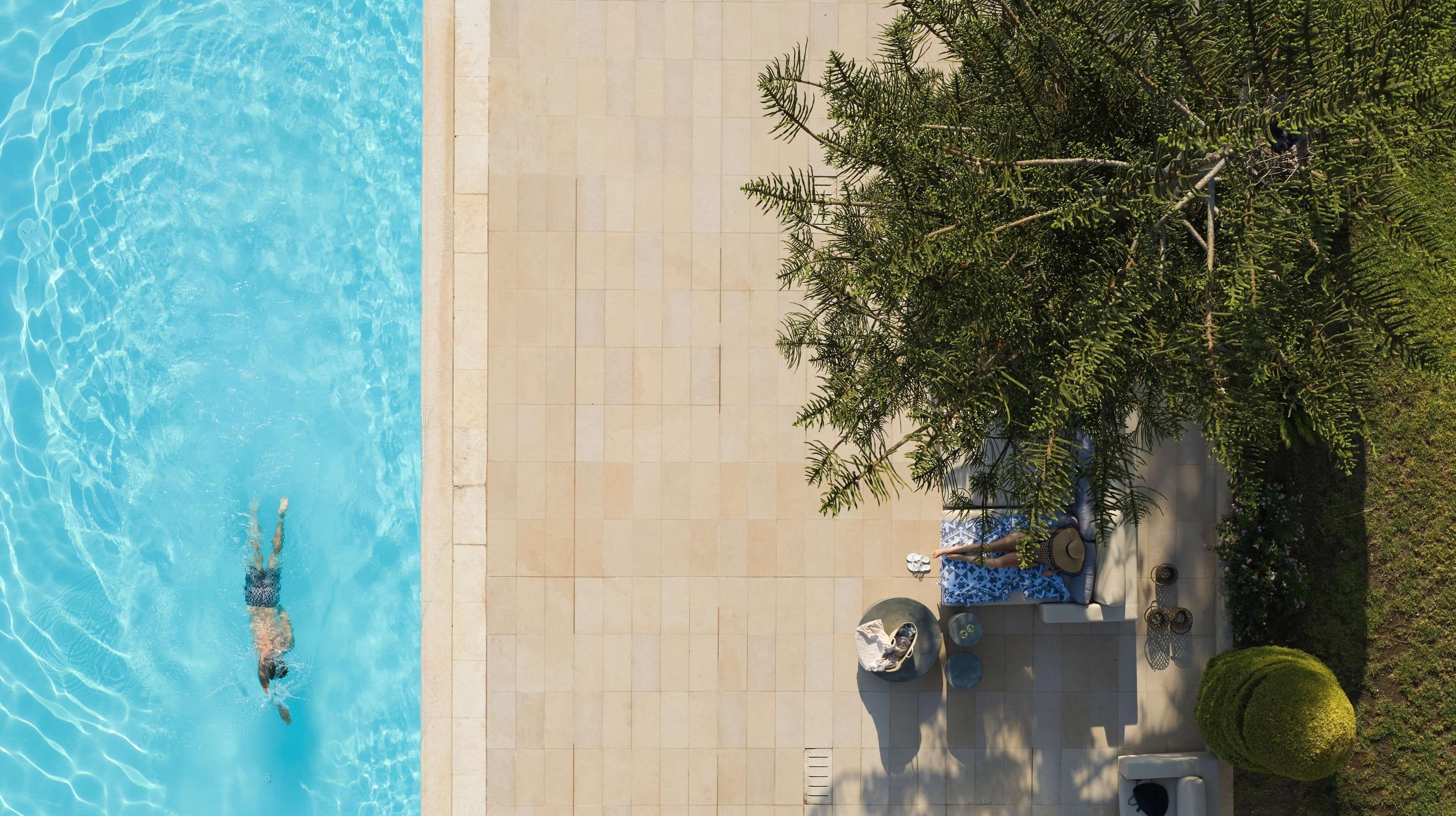 Une piscine à l’eau d’un bleu cristallin, une terrasse carrelée et un espace de détente avec un fauteuil et une table.