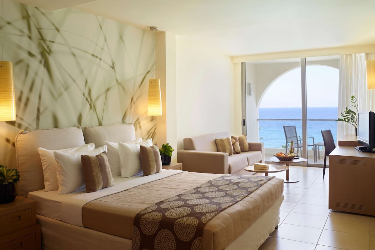 Habitación de hotel con cama, sofá, escritorio y vista al mar.