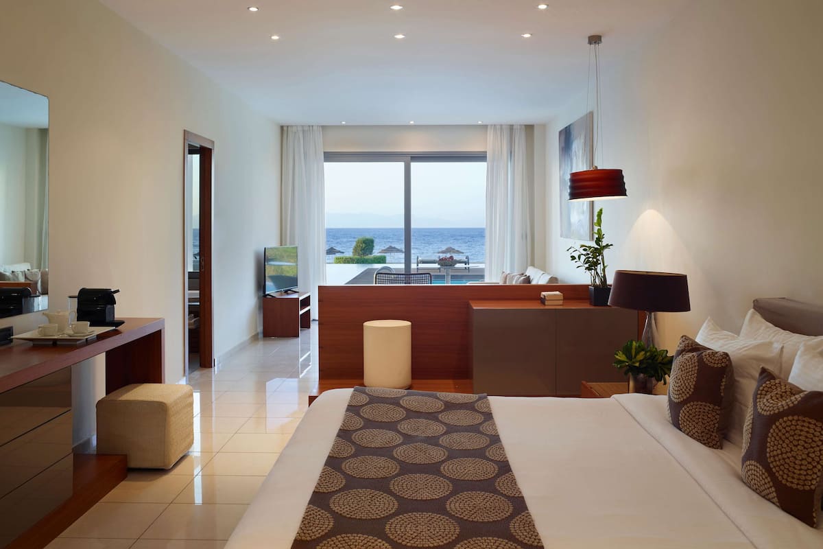 Una habitación de hotel moderna con una cama grande, un escritorio, una zona de estar y vistas al mar.