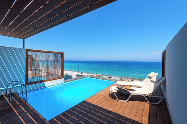 Ein Poolbereich mit Meerblick, einer Holzterrasse und Liegestühlen.