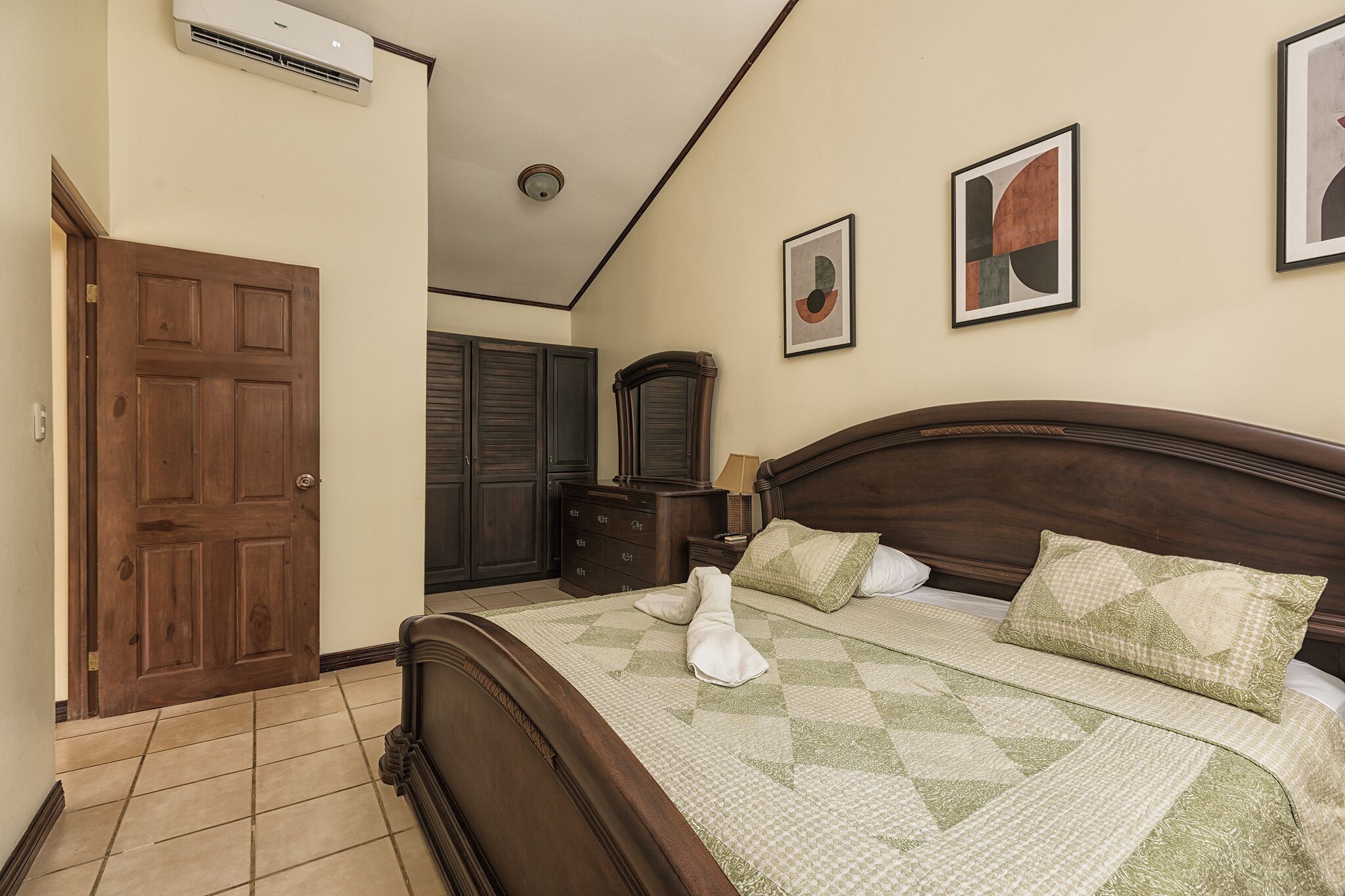 A bedroom with a wooden bed, a dresser, and two framed pictures on the wall.