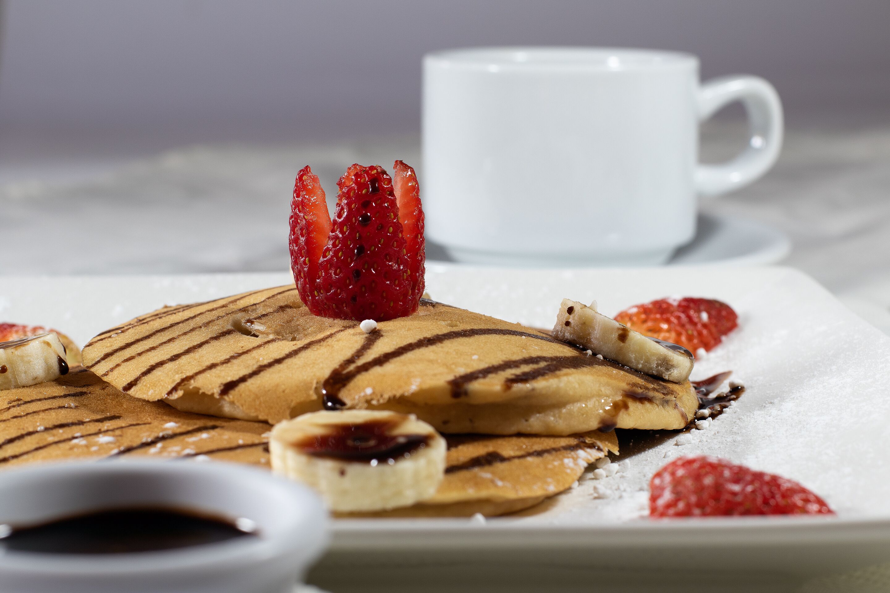 A plate of pancakes with strawberries and a small cup of syrup.