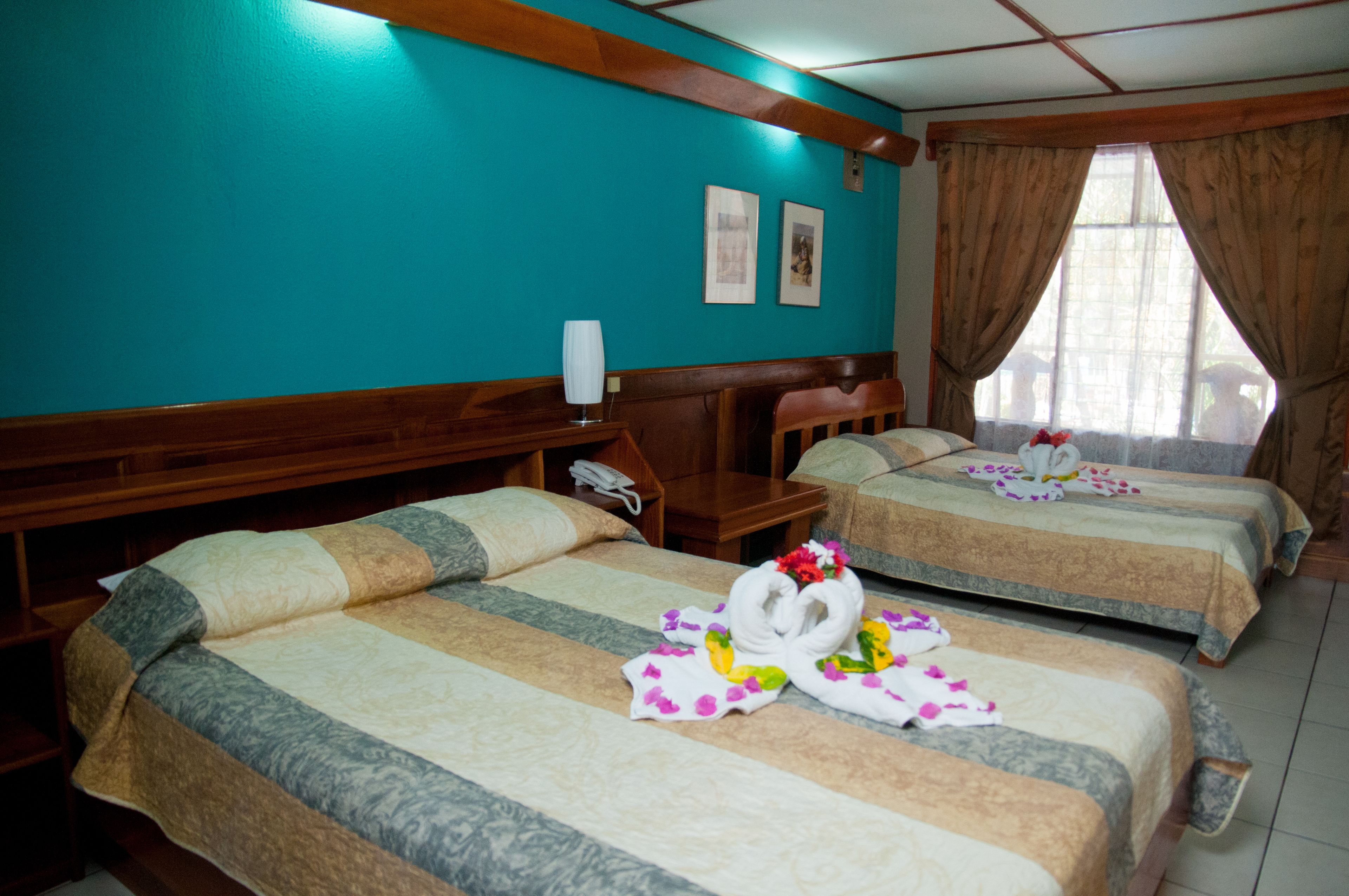 Une chambre d’hôtel avec deux lits, des têtes de lit en bois, un mur de couleur turquoise et une fenêtre avec des rideaux.