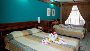 Une chambre d’hôtel avec deux lits, des têtes de lit en bois, un mur de couleur turquoise et une fenêtre avec des rideaux.