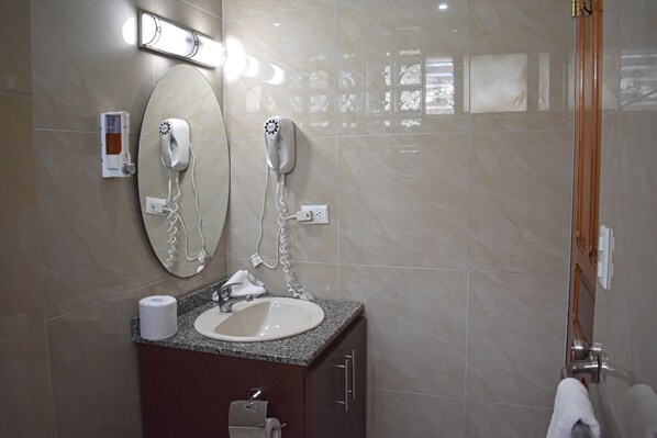 Un baño con lavamanos, espejo, secador de pelo y toallero.
