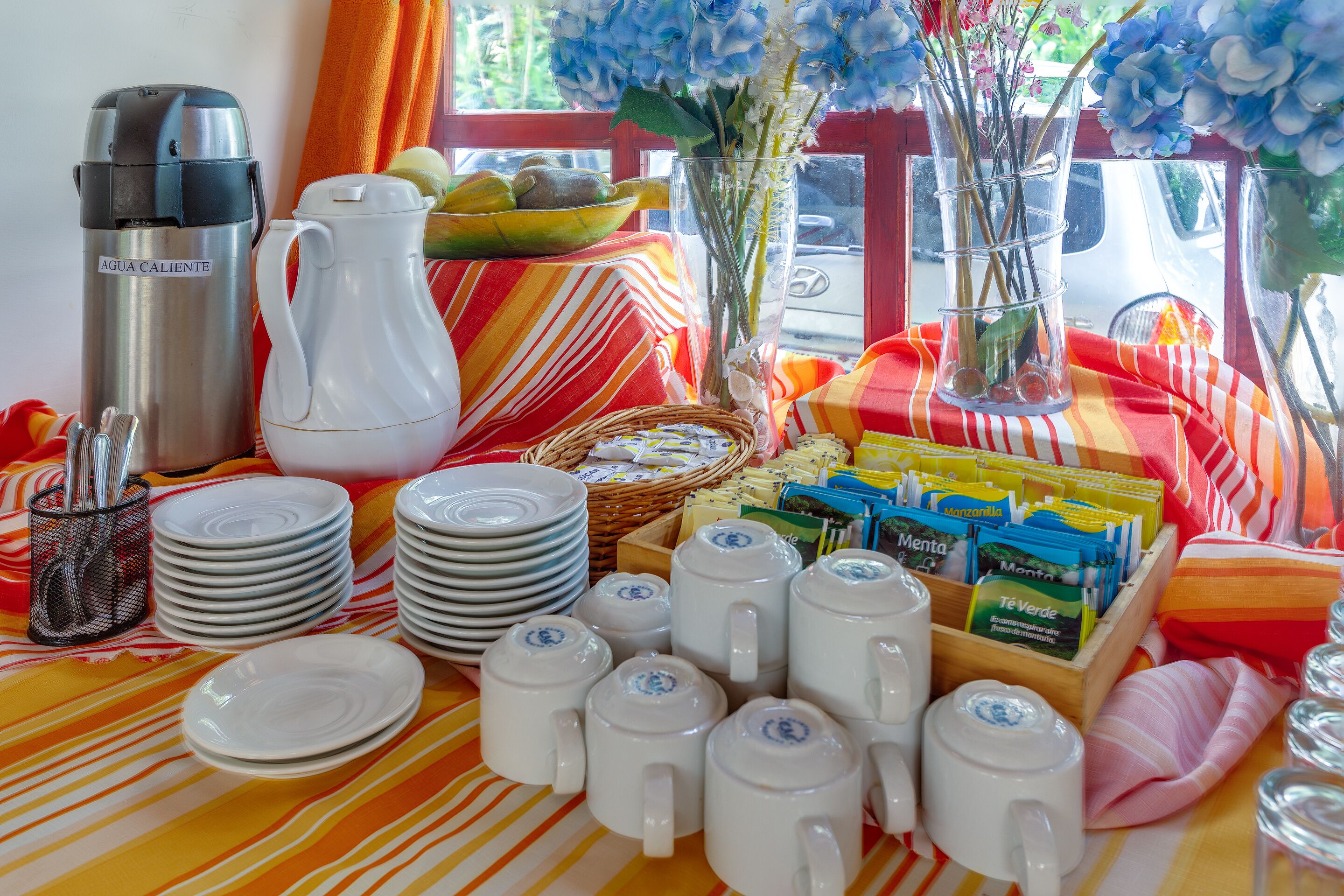 Un esmorzar preparat amb una cafetera, plats, tasses i un bol de fruita damunt d'una estovella a ratlles.