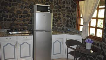 A kitchen with a stone wall, a refrigerator, a microwave, a stove, and a dining area with a chair and table.
