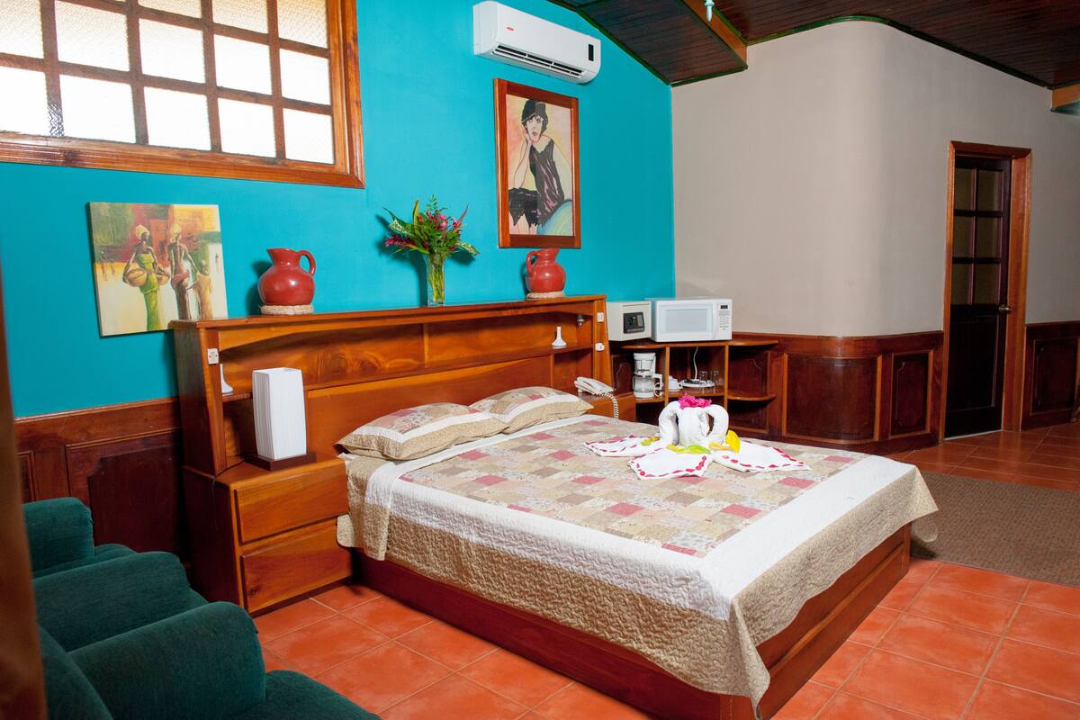 A bedroom with a wooden bed, a nightstand, a desk, a chair, and a window with a view.