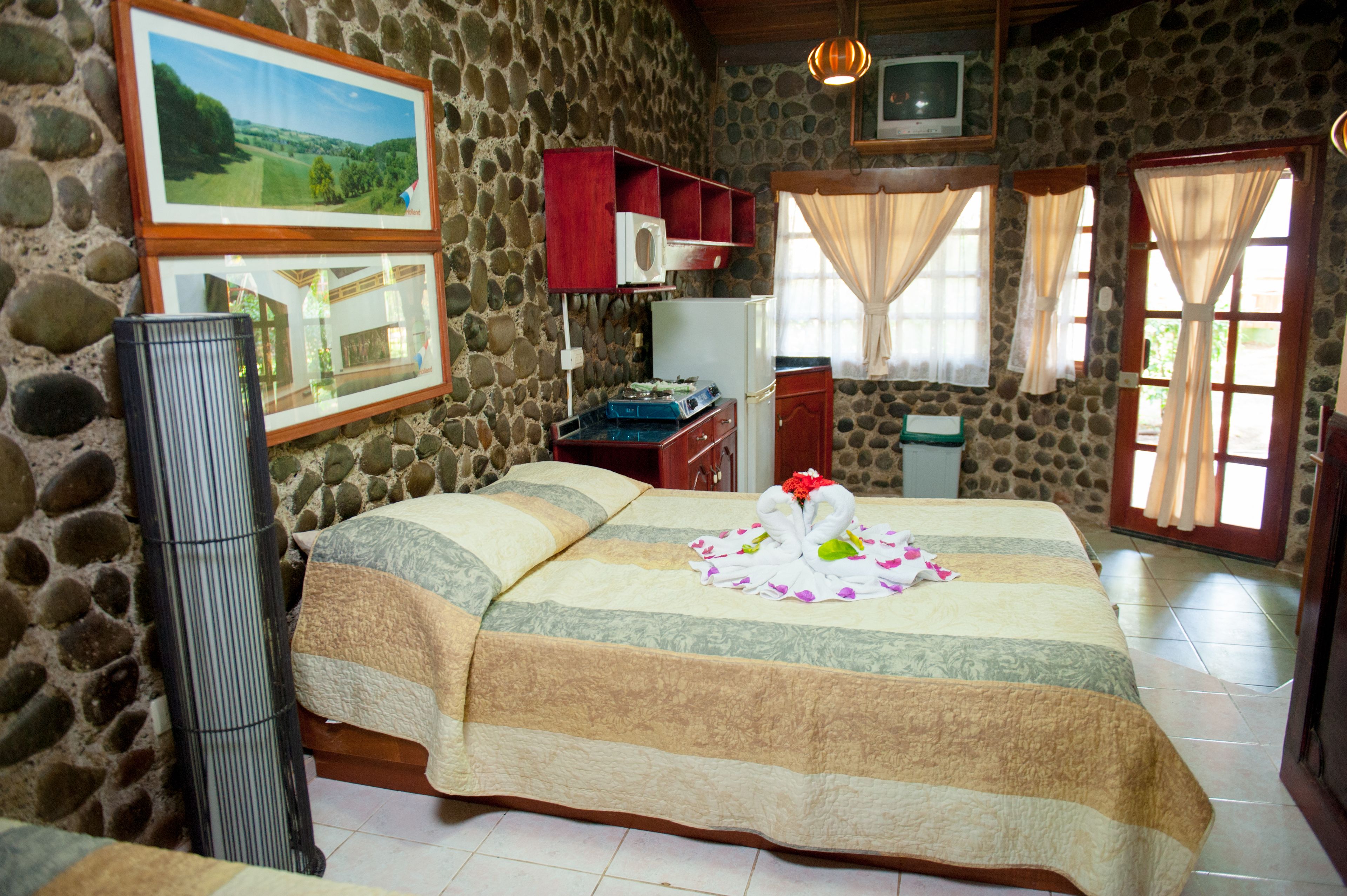 A cozy room with a stone wall, a bed with a floral bedspread, a television, and a small cabinet.