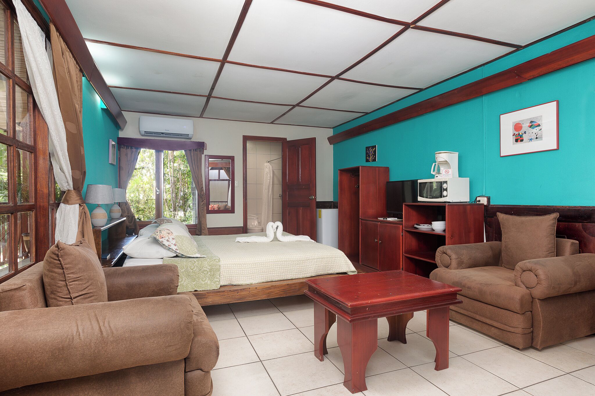 A room with a bed, two brown sofas, a wooden coffee table, a TV, and a microwave.