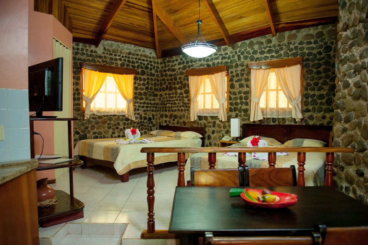 A room with two beds, a dining table, a TV, and stone walls.