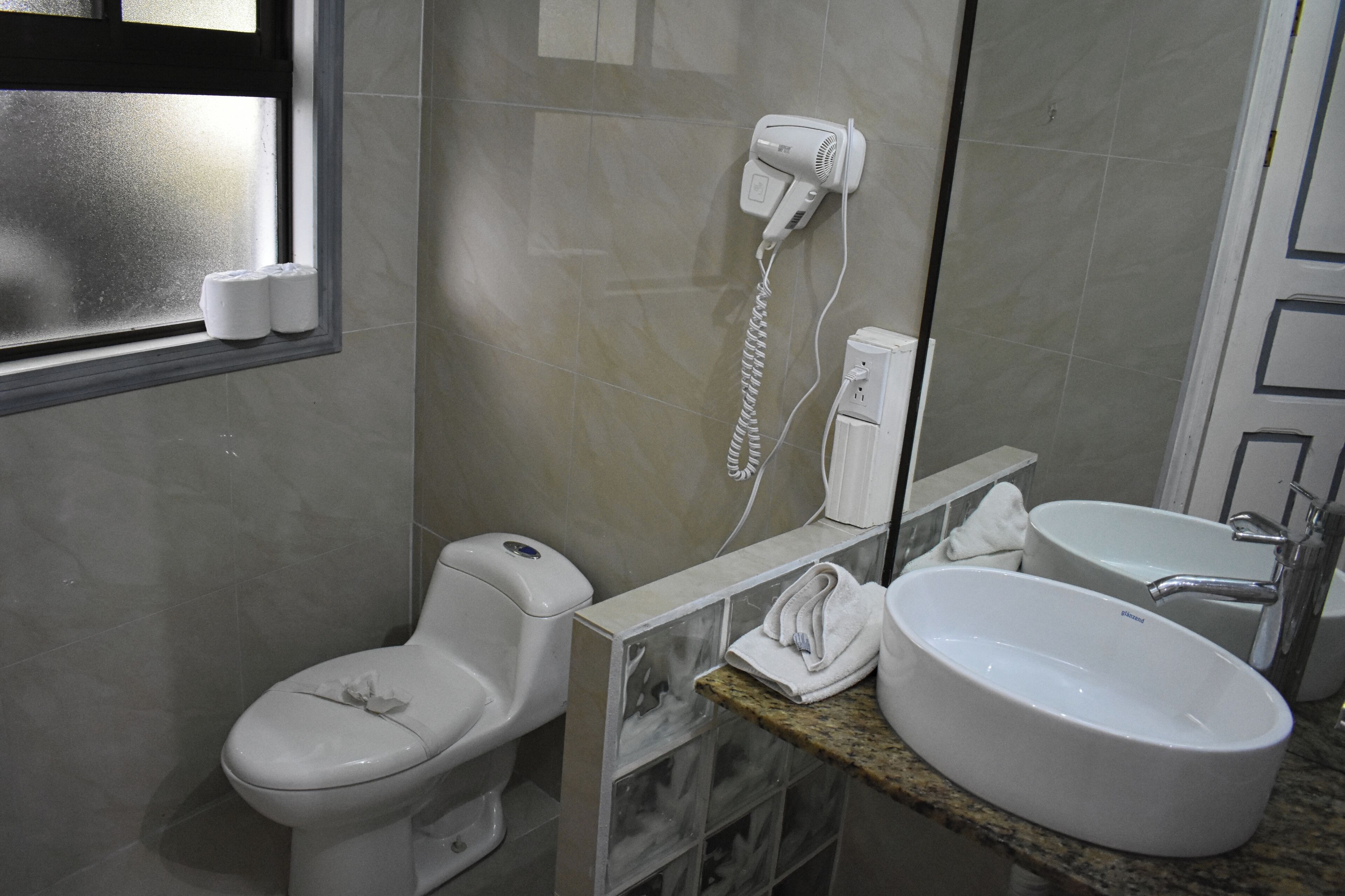 A bathroom with a toilet, a hand dryer, a sink, and a mirror.