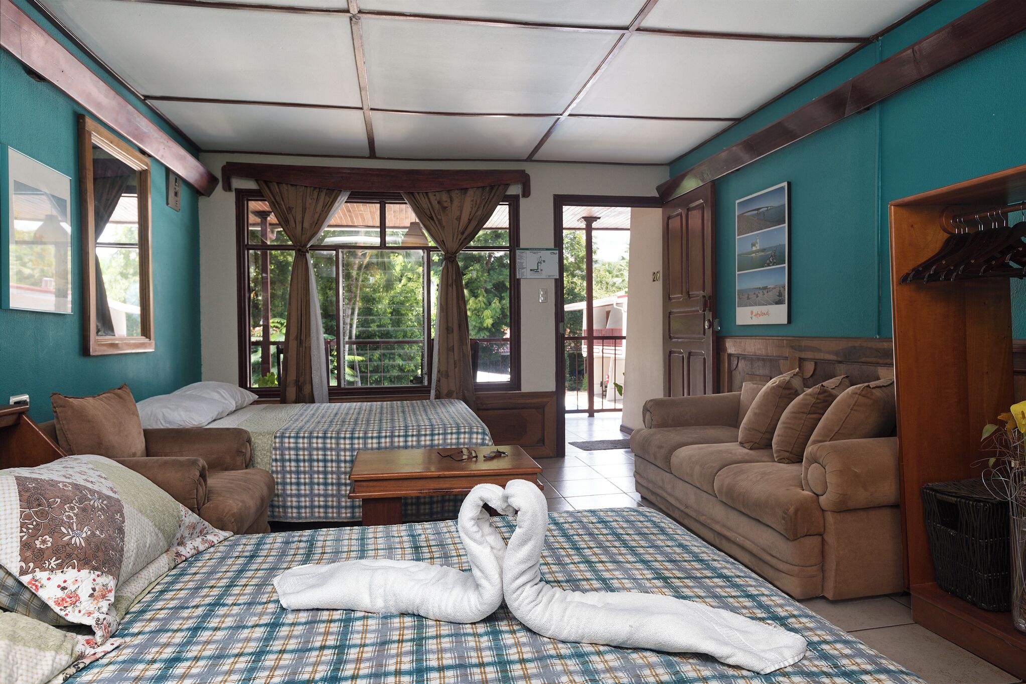 A hotel room with two beds, a sofa, a wooden table, and a view of the outdoors.
