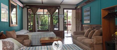 A hotel room with two beds, a sofa, a wooden table, and a view of the outdoors.