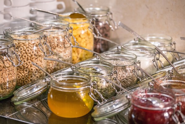 Diversos alimentos en recipientes de vidrio con cierres metálicos, como cereales, frutos secos y miel.