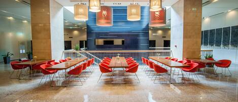 A spacious conference room with a long table and red chairs, large windows, and modern lighting fixtures.