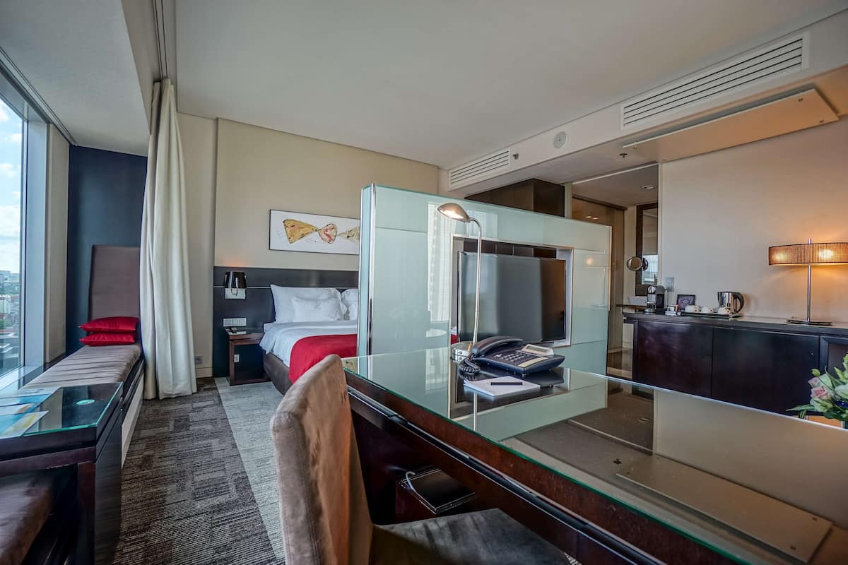 Habitación de hotel con cama, escritorio, teléfono, espejo y ventana con cortinas.
