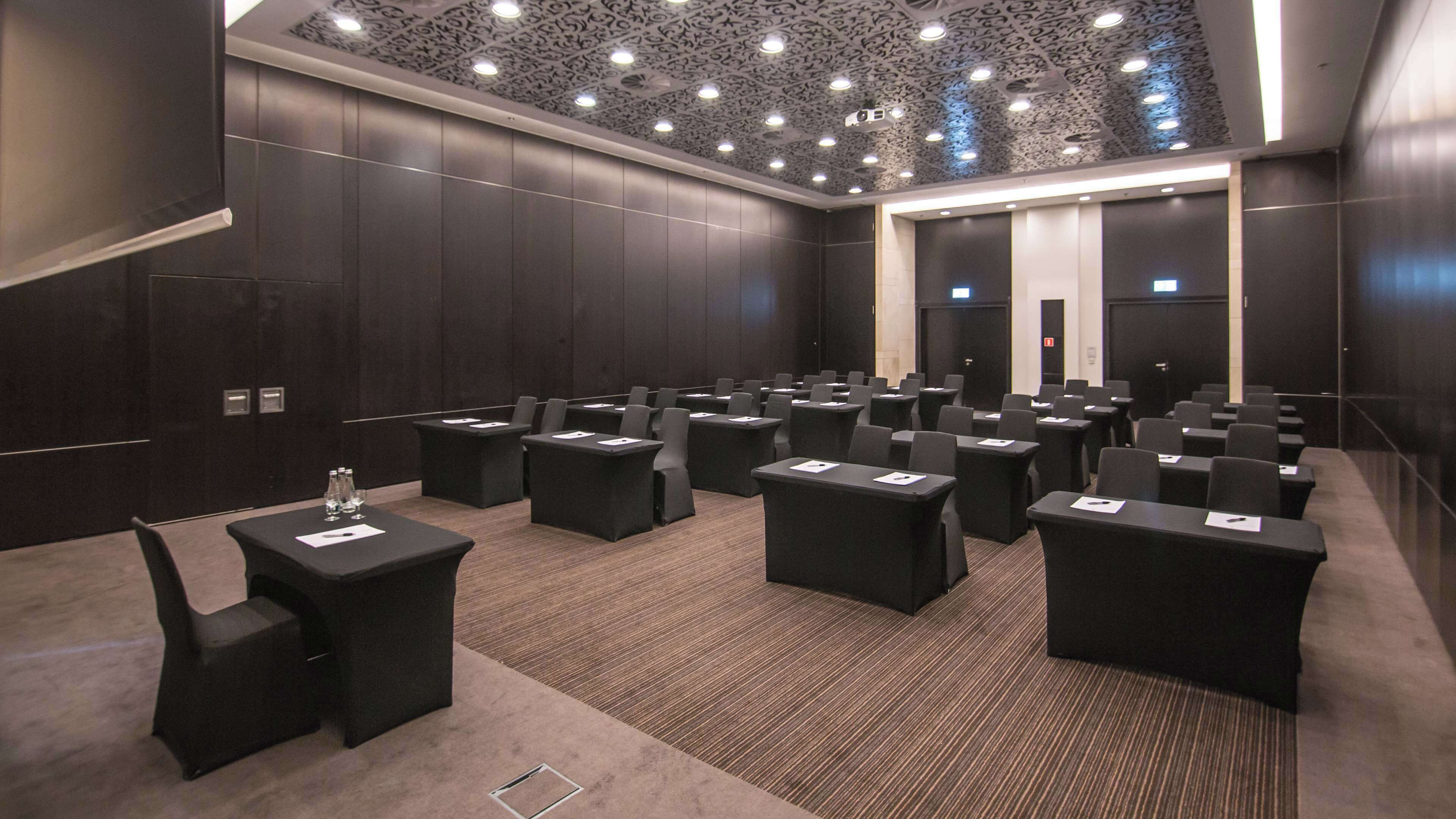 Een congreszaal met rijen tafels en stoelen, donkere wanden en een gestreept plafond.
