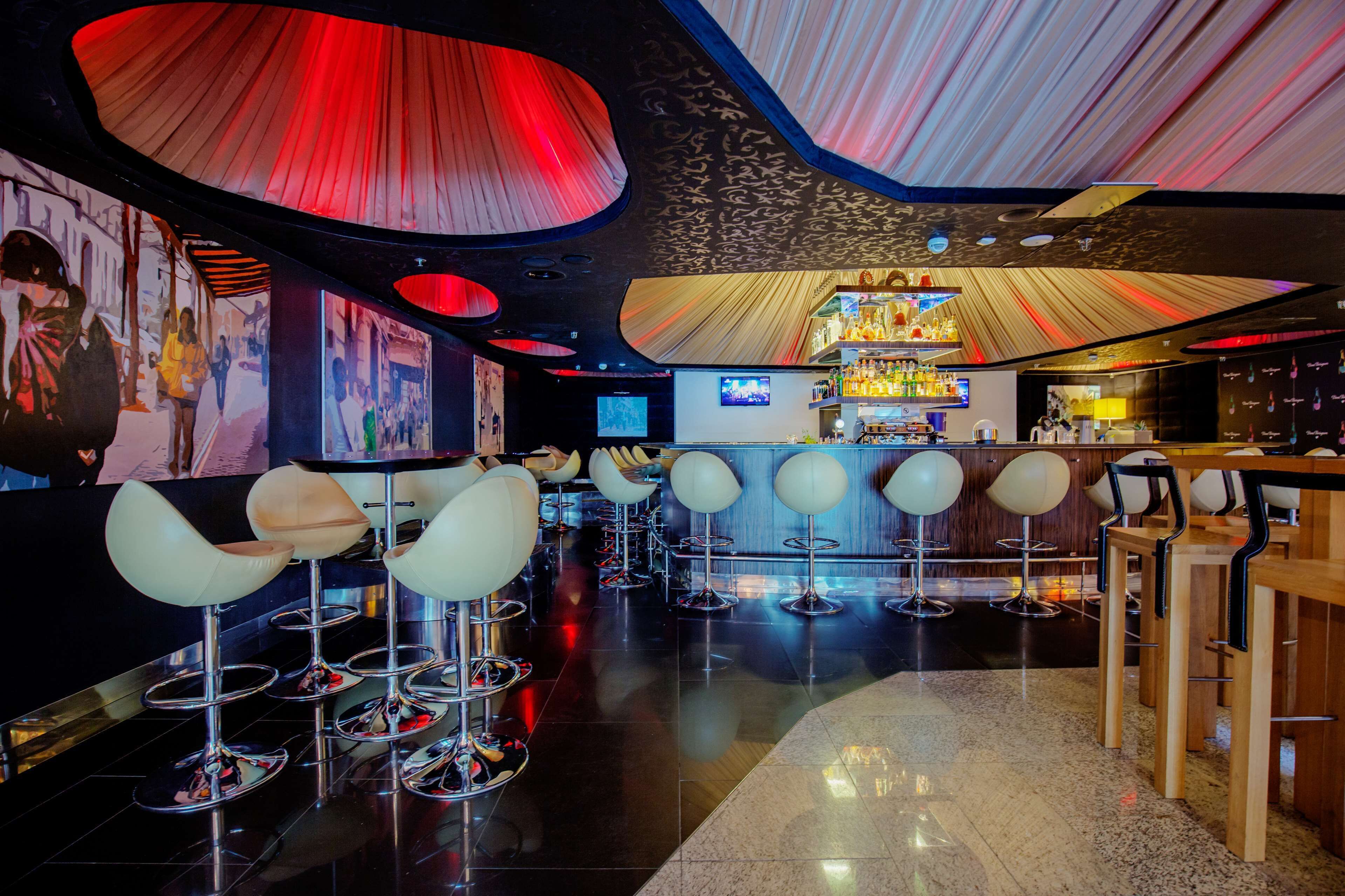 A modern bar area with high stools, a bar counter, and a television screen.