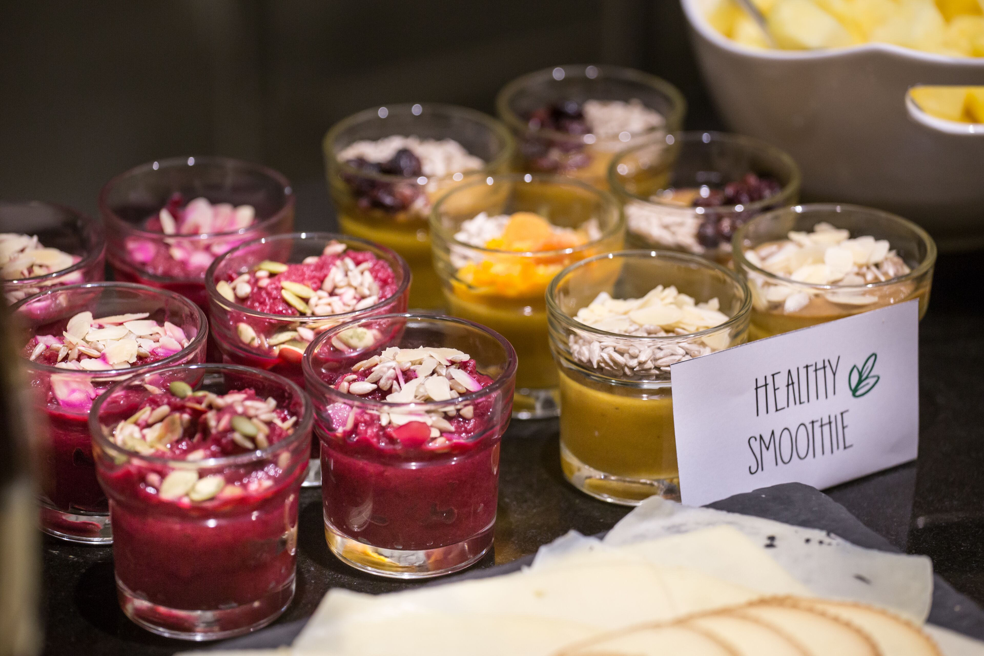 A variety of healthy smoothies in small glasses, some with fruits and nuts, and a sign indicating 'Healthy Smoothie'.