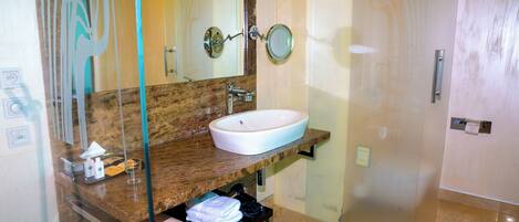 Un baño con encimera de mármol, lavamanos blanco, cabina de ducha de vidrio y toallero.