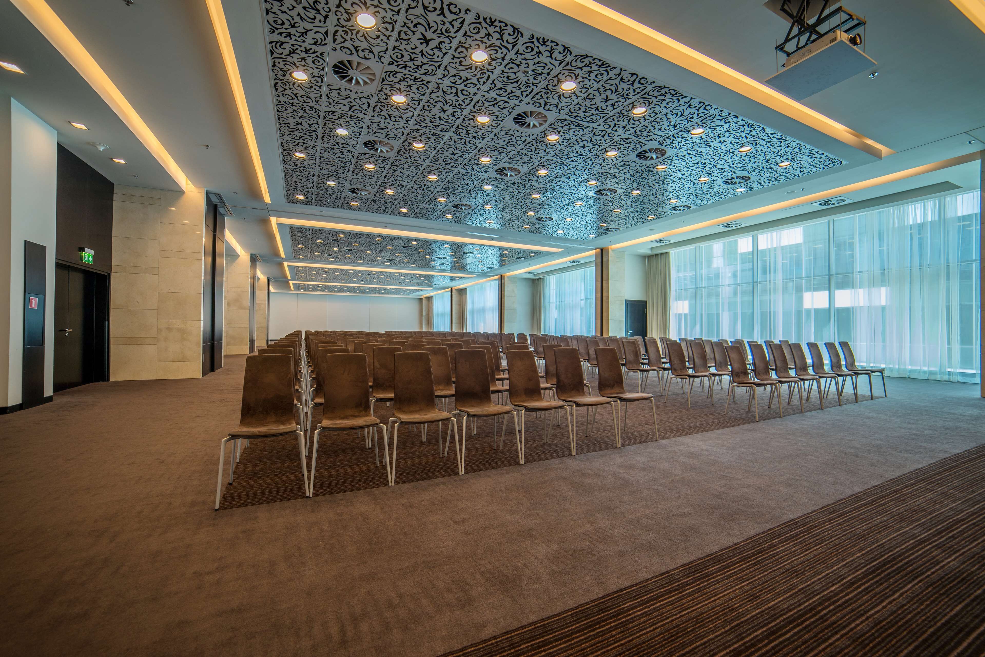 A conference room with rows of chairs, a patterned ceiling, and large windows.