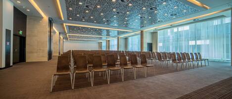 A conference room with rows of chairs, a patterned ceiling, and large windows.