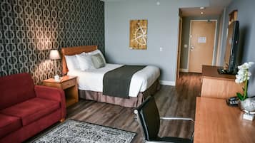 Habitación de hotel con una cama, un sofá rojo, un escritorio con espejo y un cuadro de una brújula en la pared.