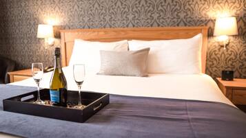 A neatly made bed with a wooden headboard, two bedside lamps, and a tray with a bottle and glasses on the bed.