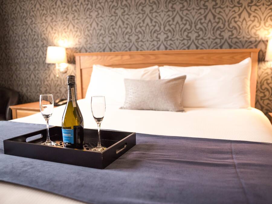 A neatly made bed with a wooden headboard, two bedside lamps, and a tray with a bottle and glasses on the bed.