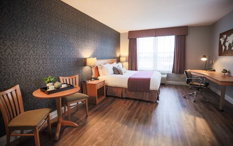 A hotel room with a bed, desk, chair, table, lamp, and a window with curtains.
