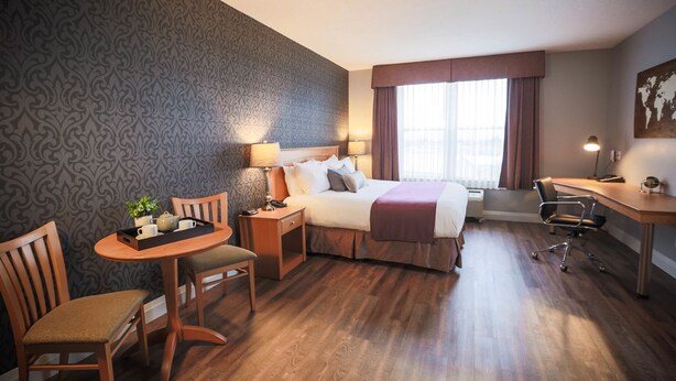 A hotel room with a bed, desk, chair, table, lamp, and a window with curtains.