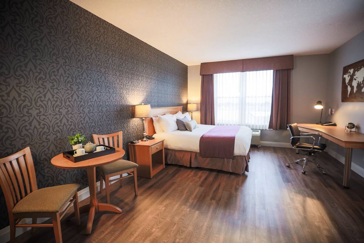 A hotel room with a bed, desk, chair, table, lamp, and a window with curtains.